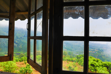 Obraz premium View through open wooden windows overlooking mist covered green mountains and tropical hills.