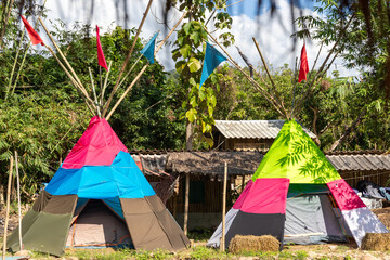 Two vibrant teepee tents decorated with flags sitting side by side at a campsite. © wannasak