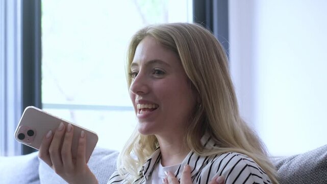 Authentic portrayal of a young blonde woman sitting on a couch, experiencing a rollercoaster of emotions from joy and laughter to worry and disbelief while talking on her smartphone