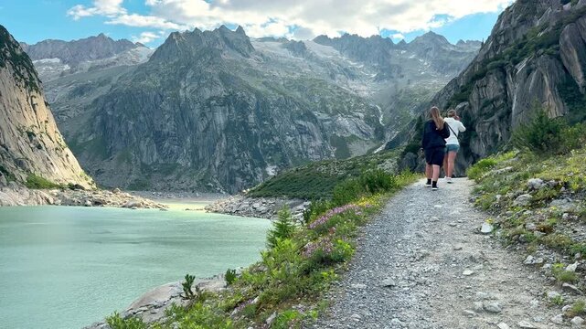 Hiker follows a rocky trail beside turquoise Gelmersee in Switzerland, Mountain lake and granite peaks create a dramatic Alpine trekking landscape