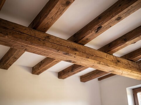 Wooden ceiling beams create a rustic, warm interior accent in a bright room with white walls and a window.