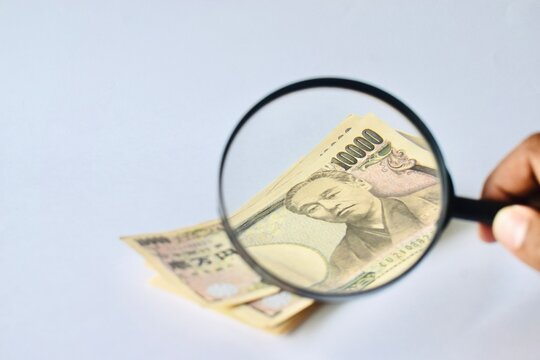 A magnifying glass inspecting a Japanese 10000 yen banknote close-up, visualizing financial scrutiny, foreign currency evaluation, and economic analysis.