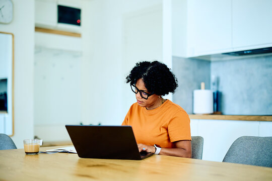 Woman focusing on laptop, typing on keyboard, working from home. Freelancer managing online business and digital tasks