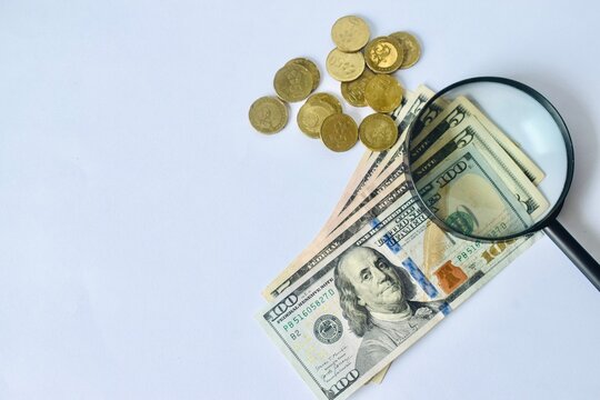 Flat lay composition of US dollars, coins, and a magnifying glass positioned on a white background with ample copy space for financial branding.