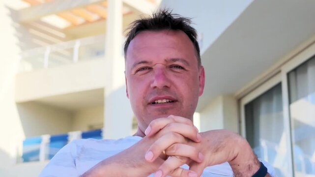 Man sitting outdoors near hotel building makes stop or rejection gesture by crossing his arms