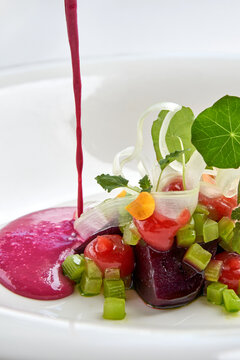 Pouring bright pink beetroot cream soup into a white bowl garnished with fresh greens and microgreens. High-end gourmet dining.