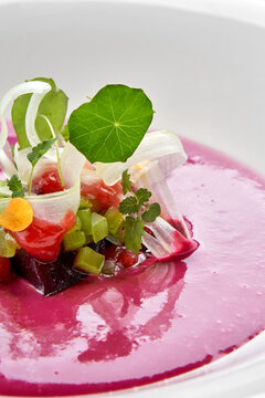 Macro extreme close-up of vibrant pink beetroot soup garnished with delicate microgreens, nasturtium leaf, and diced vegetables.