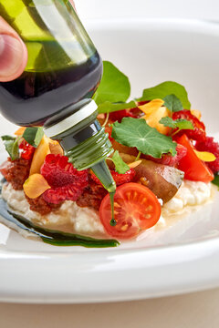 Chef dressing gourmet salad with green herb oil in white bowl, action macro shot.