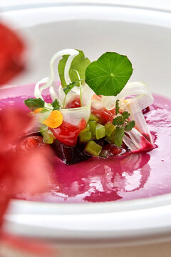 Macro extreme close-up of vibrant pink beetroot soup garnished with delicate microgreens, nasturtium leaf, and diced vegetables.