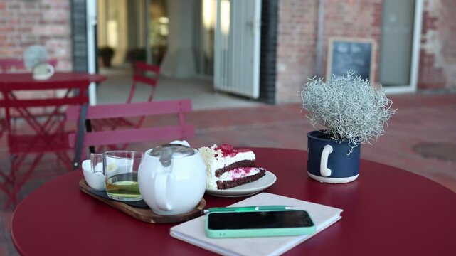 Cafe table prepared for a relaxing break with raspberry cake tea smartphone and notebook creating a basic everyday setting for enjoying dessert and planning the day ahead