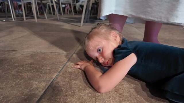 Tired young child lying on floor in public space, resting her head on ground