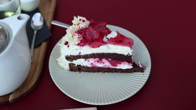Raspberry chocolate layer cake with fresh berries and creams served beside a teapot and lemon at a cafe table creating a cozy afternoon tea and dessert setting for guests
