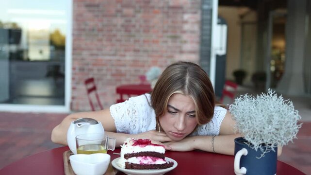 Woman stares intensely at a tempting berry cake at an outdoor cafe debating whether to eat the dessert while struggling with cravings diet choices and strong self control
