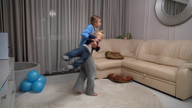 Cheerful young girl dancing and playing with her little sister in modern living room at home