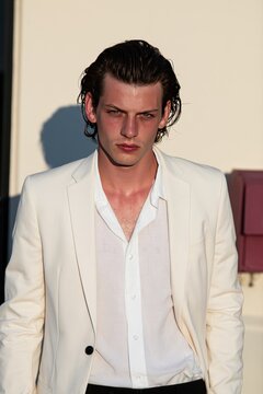 Young Man in Stylish White Suit Standing Outdoors in Warm Sunlight