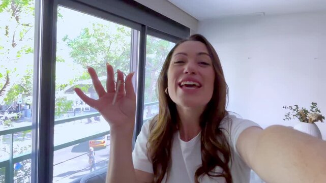 Joyful woman filming a selfie video, excitedly showing off the keys to her new apartment, celebrating the purchase of her dream home and expressing happiness for this new life chapter
