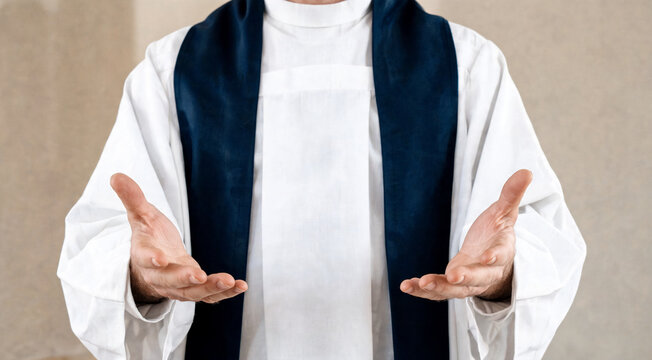 Person in white robe with hands extended, possibly leading a ceremony or service