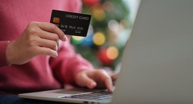 Woman holding a credit card while shopping online on a laptop during Black Friday and Christmas, representing digital payment, seasonal sales, secure checkout and festive spending.