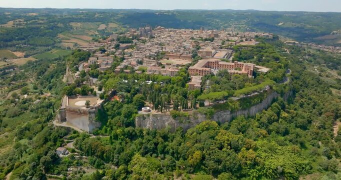Aerial panoramic view of the historic town of Orvieto perched atop its volcanic tuff cliff, in the province of Terni, Umbria, Italy, with the Rocca Albornoz gardens visible on the clifftop edge.