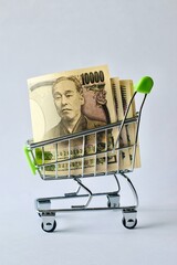 Japanese 10000 yen banknotes stacked inside a miniature shopping cart on a white background. © Akram