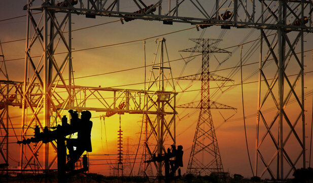 the electric workers working on pole overtime in front of group of object electric high electric pole steel structure in construction site on sunset abstract nature background