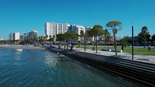 Calm harbor of Vlora, people enjoying Lungomare promenade along the seashore with flowers and palm trees