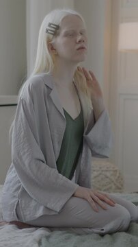 Slow motion portrait of beautiful albino woman in pajamas sitting on bed in luxurious bedroom at home. People and apartment concept.