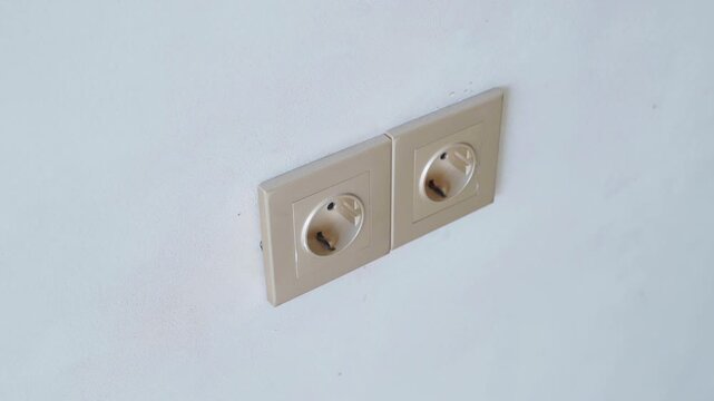 Close-up of two recessed electrical sockets mounted side by side on a light-colored wall. Beige square faceplates frame the unused outlets in a simple interior detail.