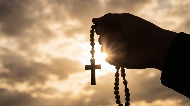 Silhouette of a hand holding rosary beads with a cross against a dramatic sunset sky.