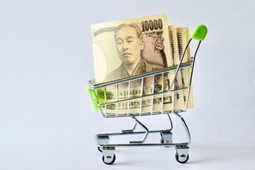Japanese 10000 yen banknotes stacked inside a miniature shopping cart on a white background. © Akram