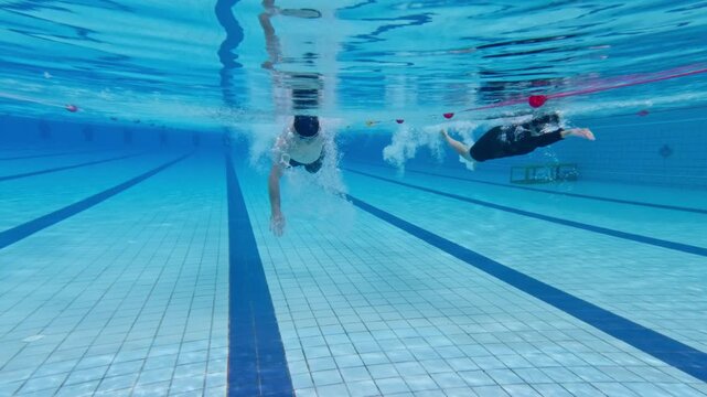 Athletic sportsman and woman swimming side by side in an outdoor pool. 