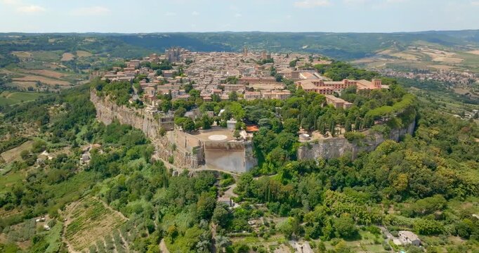 Aerial panoramic view of the historic town of Orvieto perched atop its volcanic tuff cliff, in the province of Terni, Umbria, Italy, with the Rocca Albornoz gardens visible on the clifftop edge.