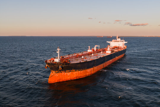 High angle aerial drone shot of a large empty cargo ship riding high in ballast on the open waters of the Baltic Sea during sunset.