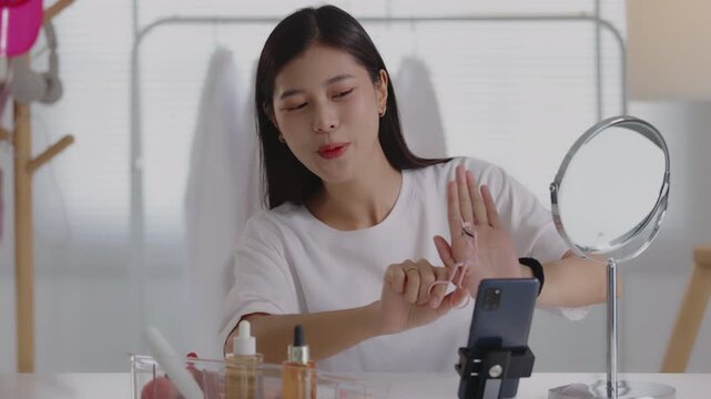 Young Asian beauty vlogger using an eyelash curler while recording makeup tutorial on smartphone.