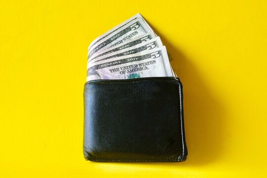 US dollar banknotes fanned out inside a black leather wallet on a bright yellow background.