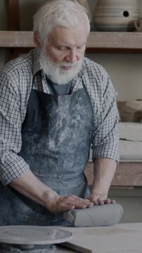 Experienced male potter mixing and kneading clay on table while working in studio with professional equipment and handmade ceramic figures