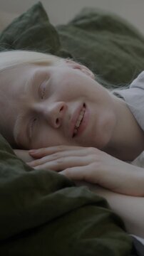 Carefree young albino woman lying in bed in pajamas enjoying rest and comfort smiling in cozy bedroom. People and relaxation at home concept.