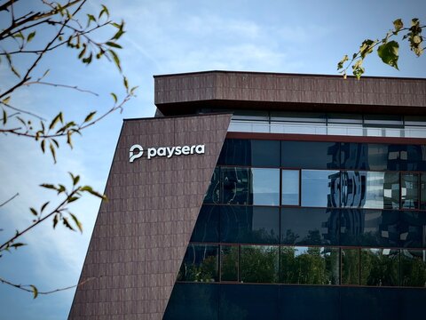 Low-angle photo of the Paysera logo on a modern corporate building facade framed by green leaves in Vilnius, Lithuania. Ideal for stock photo needs related to fintech, online payments, digital banking