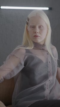 Slow motion of elegant albino woman turning to camera sitting in luxurious armchair in apartment. Individual style and glamour concept.
