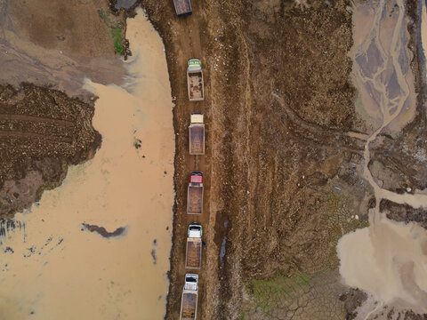 Trucks Waiting in Line at Muddy Off-Road Terrain in a Large-Scale Rock and Sand Quarry, Construction and Mining Site view from above.