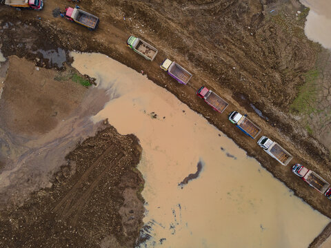 Trucks Waiting in Line at Muddy Off-Road Terrain in a Large-Scale Rock and Sand Quarry, Construction and Mining Site view from above.