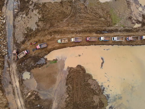 Trucks Waiting in Line on Muddy Off-Road Terrain at a Large-Scale Rock and Sand Quarry, Heavy Mining Vehicles Support Active Construction and Raw Material Extraction Operations view from above.