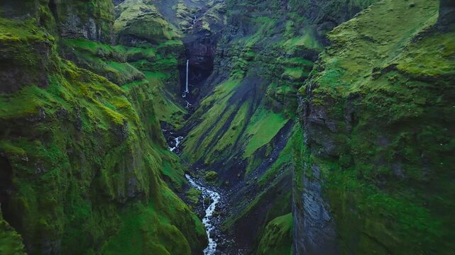Cinematic drone flight through the lush Mulagljufur Canyon revealing towering moss-covered cliffs, cascading waterfalls and a winding river deep within Iceland&rsquo;s spectacular Highlands.