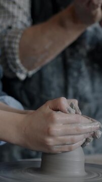Close-up of boy's hands molding clay on pottery wheel while adult teacher giving instructions in studio. Childhood and professional education concept.