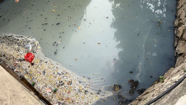 polluted stagnant urban drainage river with dirty trash and greasy texture water surface