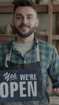 Slow motion of successful young potter holding Yes we are open sign welcoming clients opening pottery studio. Start-up and traditional arts concept.