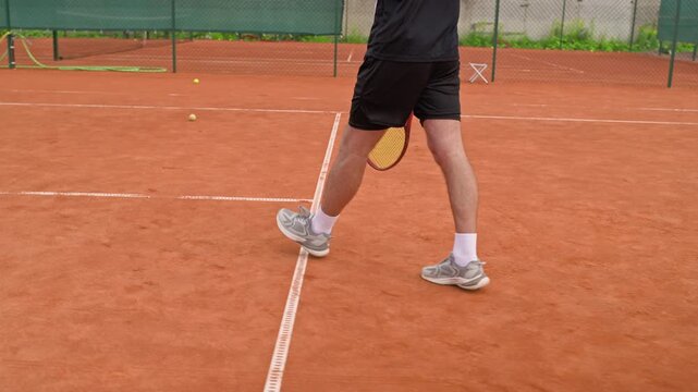 Caucasian young adult male tennis player walking on clay court holding racket in slow motion rear tracking shot. Perfect for athletic brand advertising and sports promos