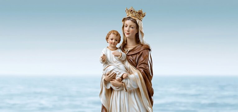 A gracefully arranged ceramic statue of Our Lady of Mount Carmel holding infant Jesus with a brown scapular, softly framed by a maritime backdrop.