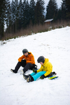 Two friends enjoy a winter day on the snowy slopes, taking a break and sharing laughs, amid the evergreens and a cozy cabin in the distance