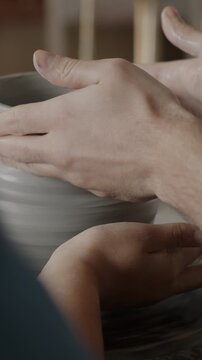 Close-up of hands man and woman making vase from clay using pottery wheel together in workshop. Enjoyable hobby and leisure activity concept.